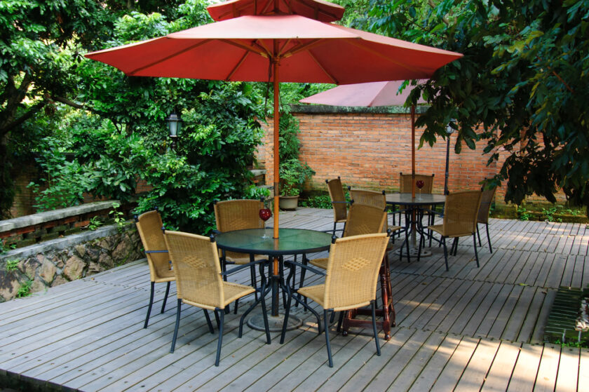 Summer Patio with tables and wooden chairs under umbrella in garden