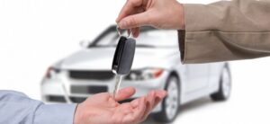 person handing over a set of car keys with white car in background