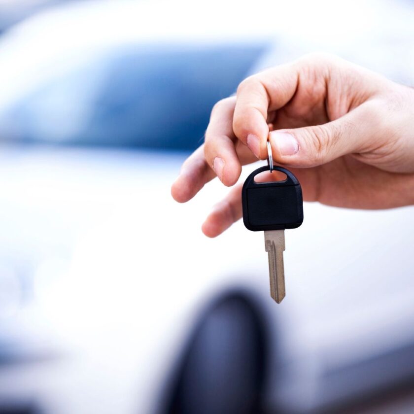 person holding a car key close to the camera with white car in the background 