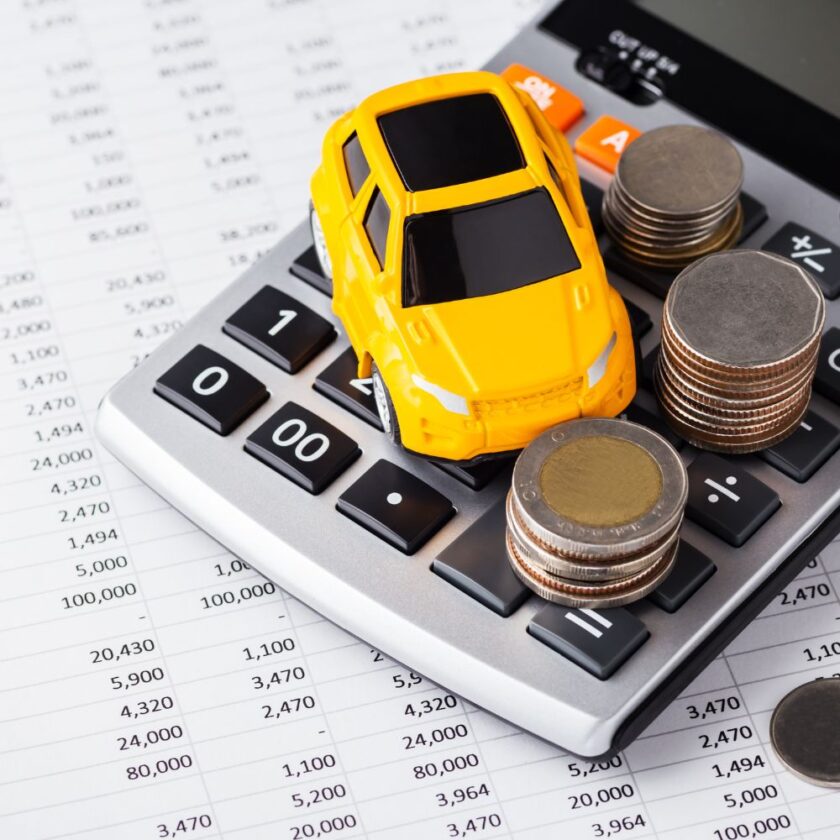 small yellow model car set on a calculator next to coins