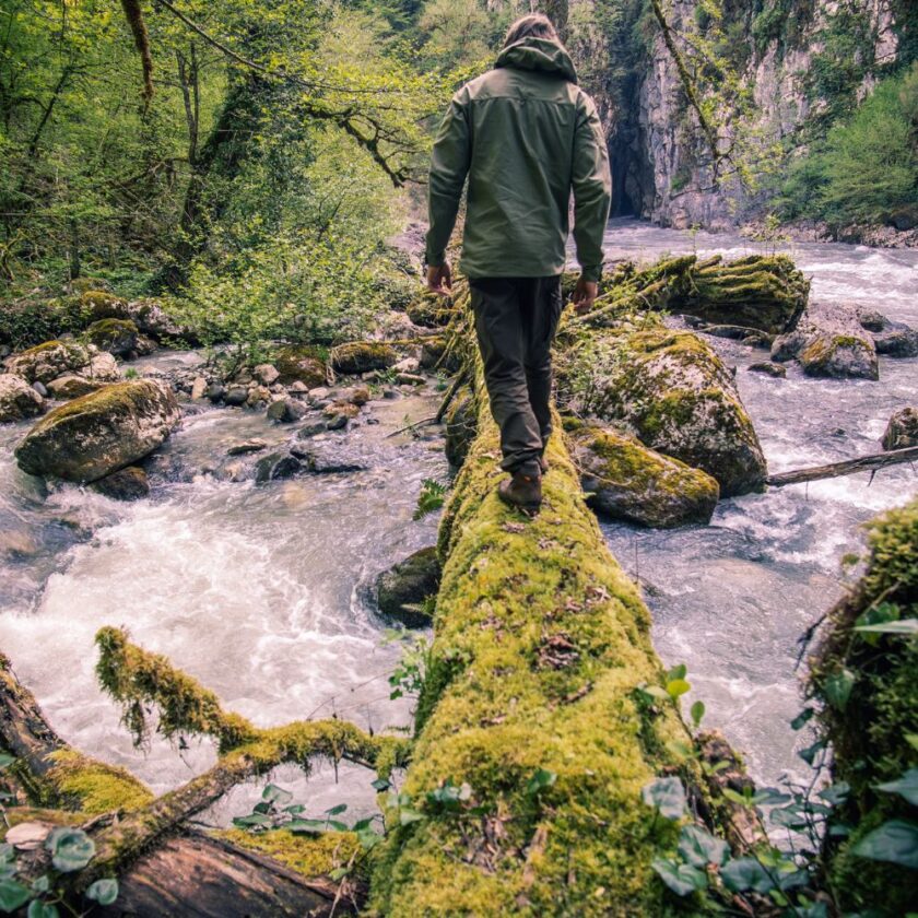 man walking across a log above flowing water