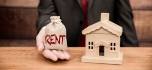 person holding a bag saying rent in one hand next to a small model house