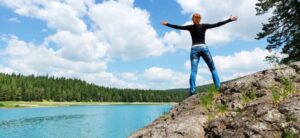 person stood on a rock with their arms out by an expanse of water