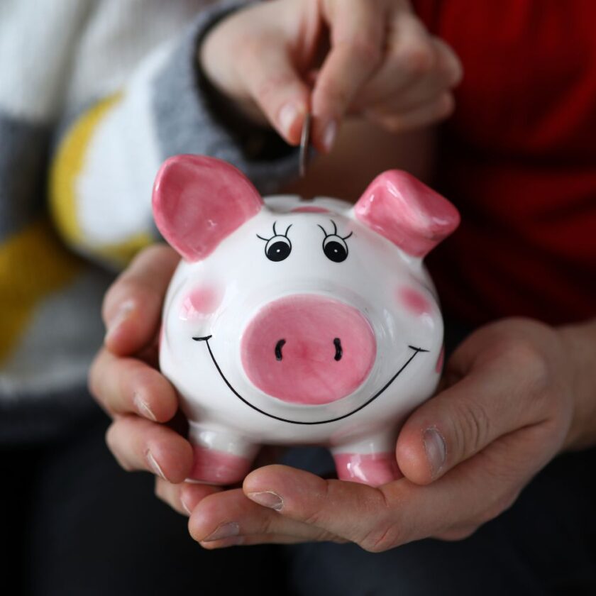 Person putting a coin into a pink and white piggy bank