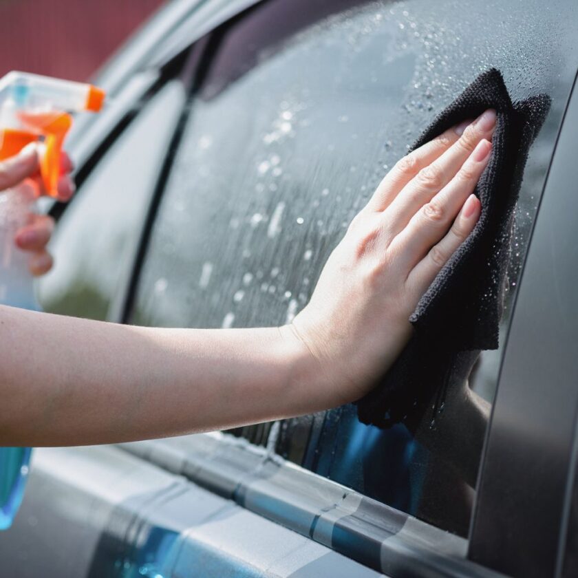 person cleaning a car with a cloth and spray
