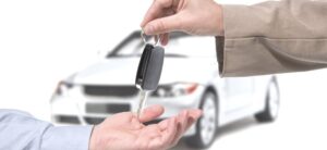 person handing over a car key to another person with a white car in the background