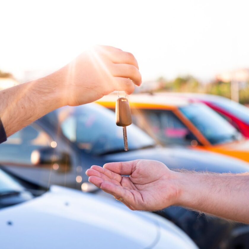 person passing a car key over with cars in the background