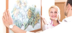 couple hanging framed art on the wall