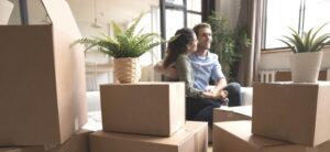 young couple sat behind packed boxes in first home