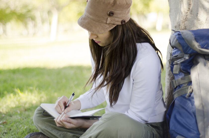 Woman sat by a tree writing in a journal