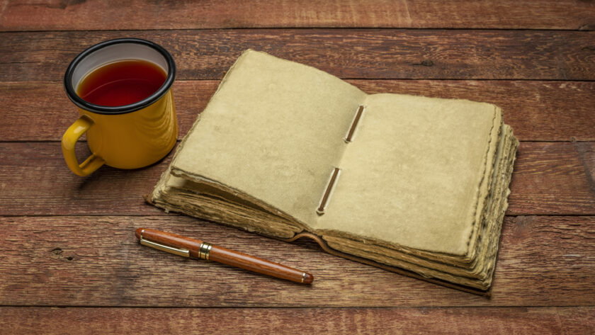 antique leatherbound journal with decked edge handmade paper pages and a stylish pen on a rustic wooden table with a cup of tea, journaling concept