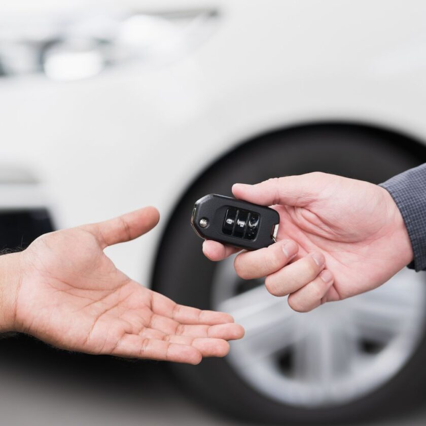 car key being passed between hands with a car in the background 