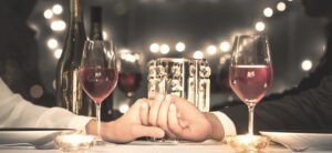 couple sat at a dinner table holding hands with glasses of wine