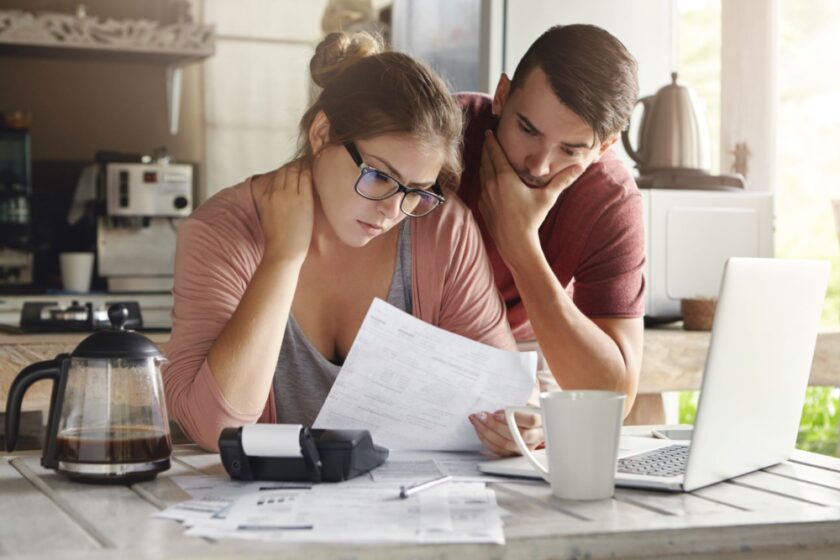 A couple sat in front of a computer looking at a sheet of paper.