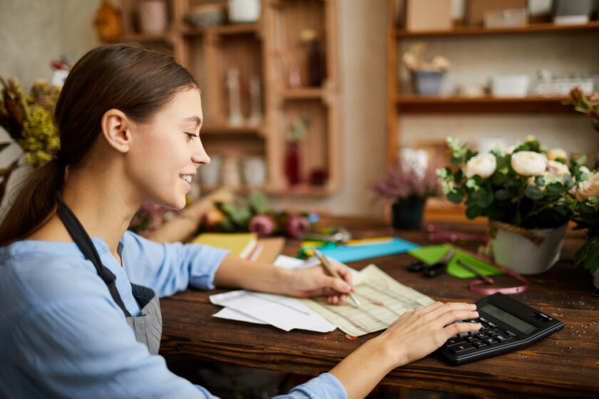 Side view portrait of female businesswoman counting finances using calculator in small shop