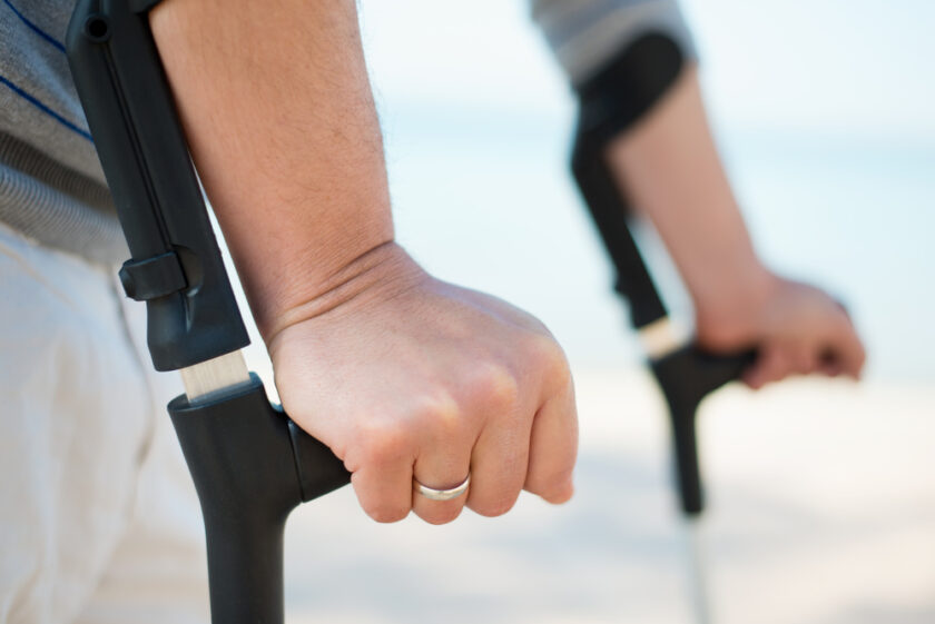 Injured Man Trying to walk on Crutches at a beach