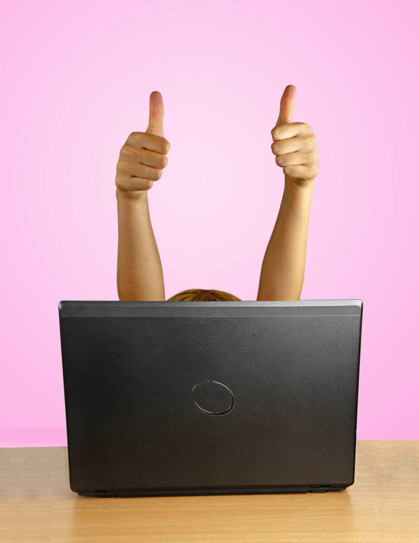 Person holding their thumbs up behind a laptop