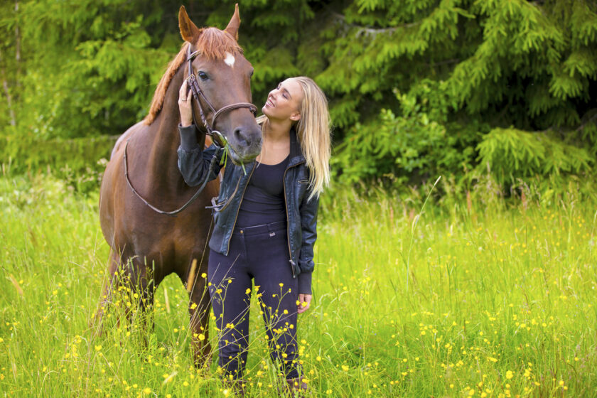 Beautiful young woman with her adult arabian horse standing in the field. Relationship between human and animal.