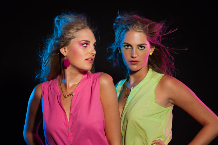 Two retro 80s fashion girls with long blonde hair. Twin sisters together.