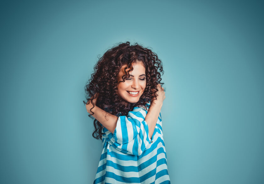 Closeup portrait confident smiling woman holding hugging herself isolated blue wall background. Positive human emotion, facial expression, feeling, reaction, situation, attitude. Love yourself concept