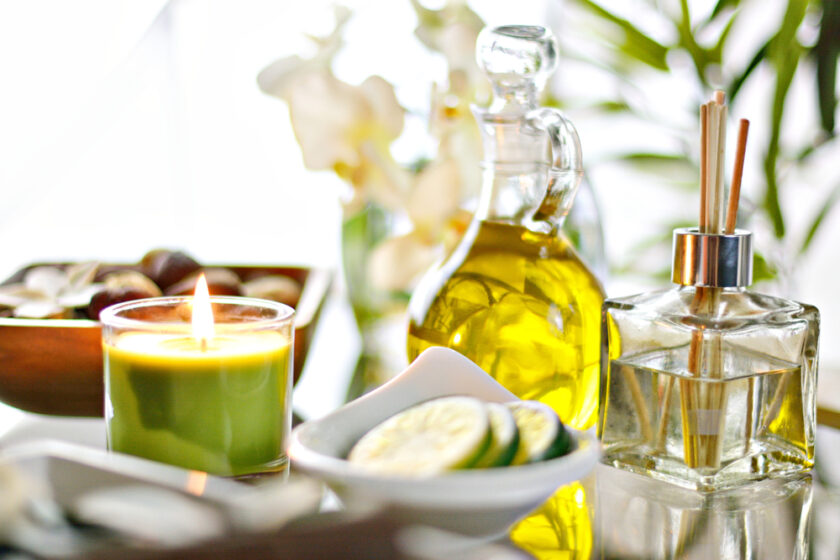 Spa setting with candle, incense, cucumbers, jojoba oil, fragrance, and flowers