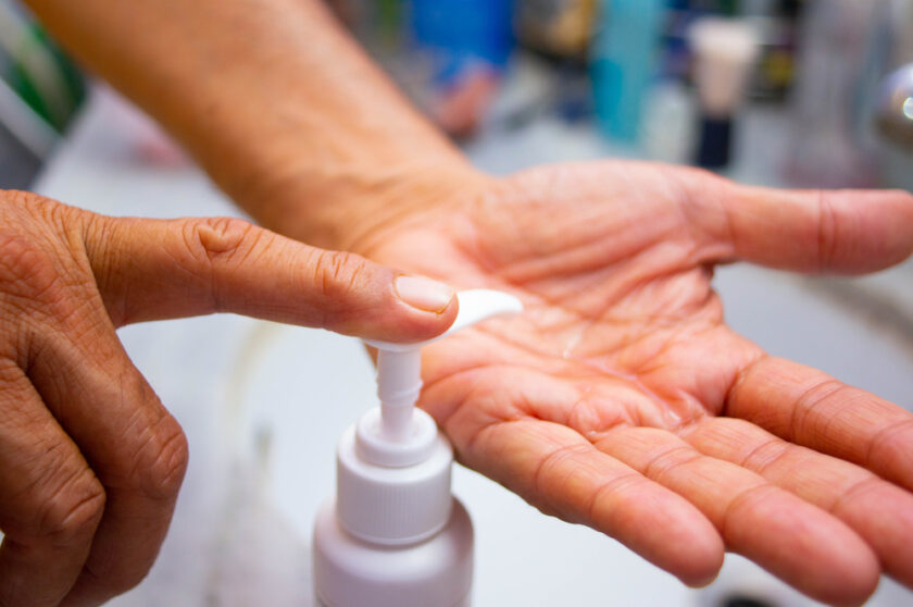 A closeup photograph the hand of a person while he is applying liquid soap or sanitizer on his hands before washing them