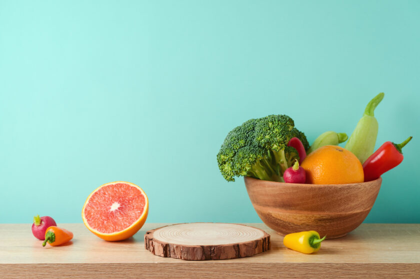 Empty wooden log with vegetables and fruits on table over blue wall background. Vegetarian kitchen interior mock up for design and product display