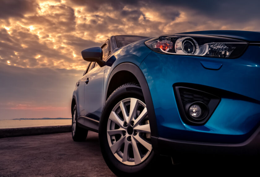 Blue SUV car with sport and modern design parked on concrete road by the sea at sunset in the evening. Hybrid and electric car technology concept. Automotive industry. Headlamp