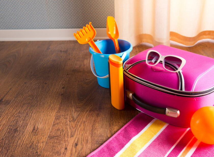 Pink bag, sunglasses, towel, sun creams and beach plastic toys on hardwood floor.