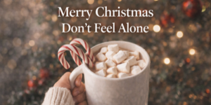 A hand holding a mug of hot chocolate with marshmallows and two candy canes. Festive lights and ornaments blur in the background. Text reads: “Merry Christmas Don’t Feel Alone.”.
