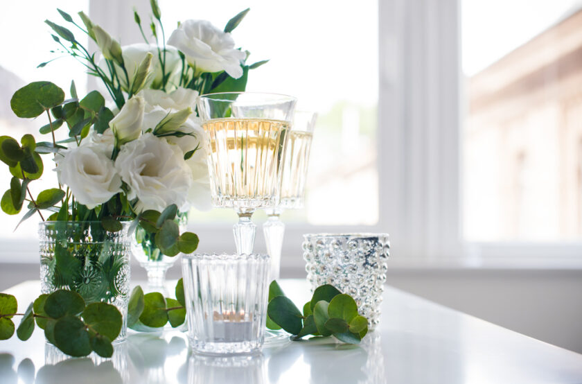 Two glasses of champagne and white flowers, candles on white table. Festive summer party decor.