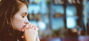Woman with her eyes closed and her hands clasped together.