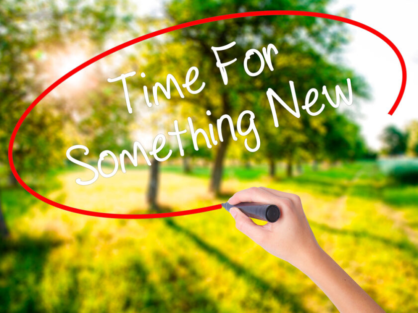 Woman Hand Writing Time For Something New on blank transparent board with a marker isolated over green field background. Business concept. Stock Photo