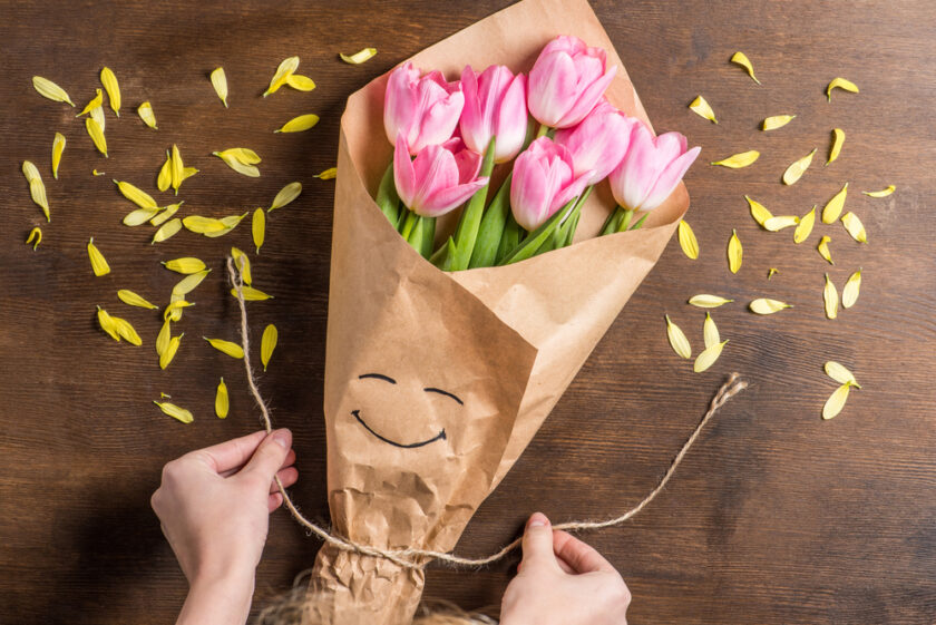 Bouquet of pink flowers wrapped in brown paper and being tied up with string