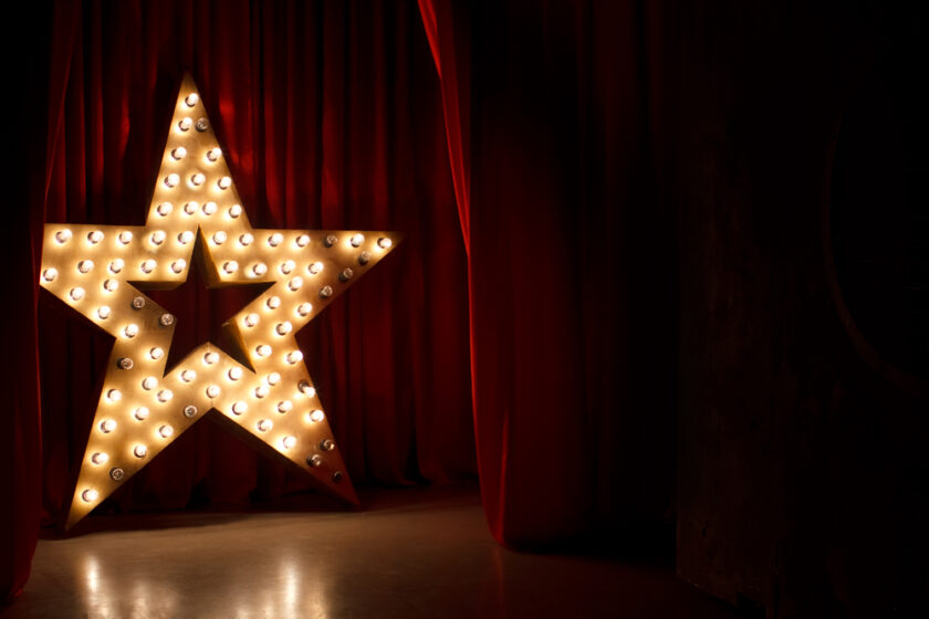 Photo of golden star with light bulbs on red velvet curtain on stage