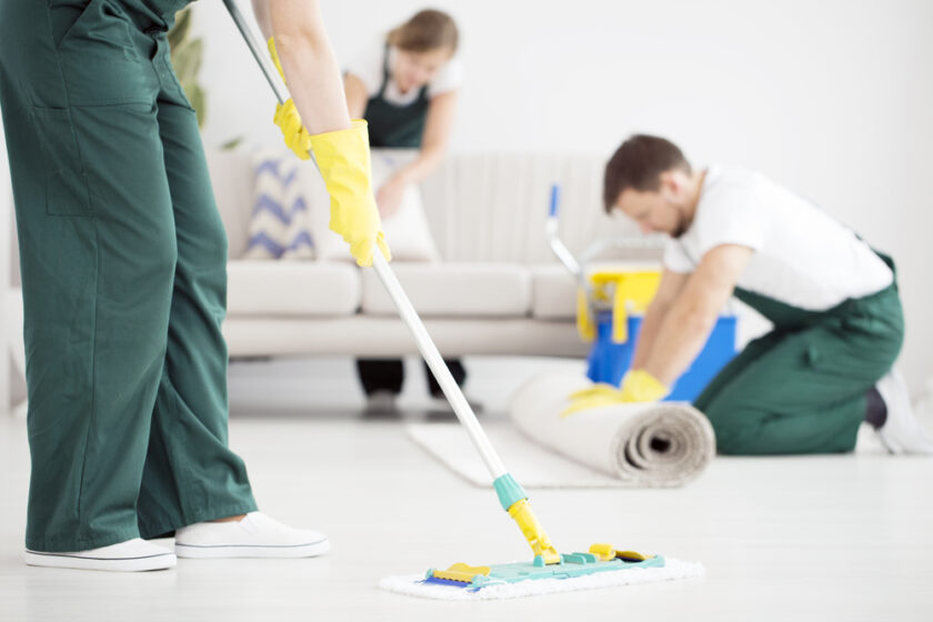 Cleaner in green overalls cleaning the floor using a mop in bright flat
