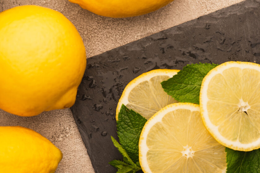 slices of lemon on a cutting board with lemons behind 
