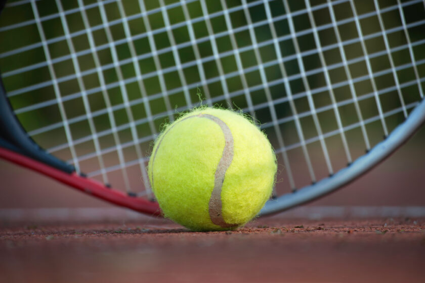 Tennis racquet and yellow tennis ball near white line, outdoor court tennis scene in low angle view