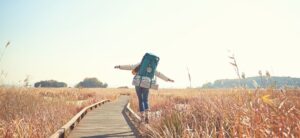 woman walking in a field along a track wearing a backpack