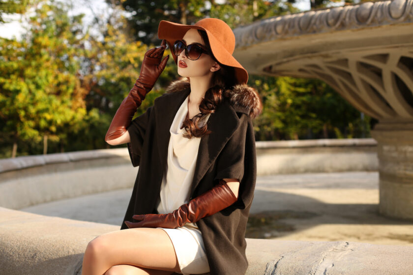 fashion outdoor photo of gorgeous sensual woman with dark hair in elegant luxurious coat, wool hat and leather gloves, walking by autumn city
