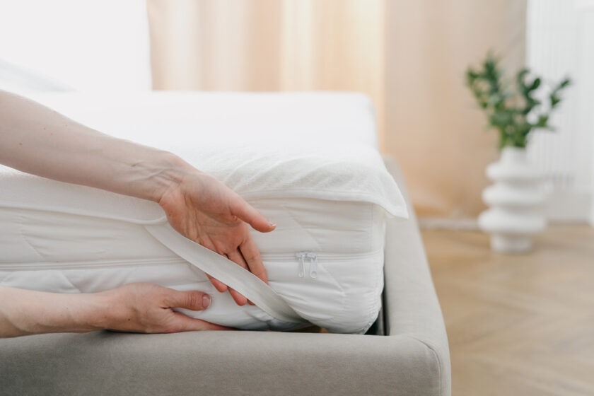 Cropped view of woman change waterproof bedding topper on orthopedic mattress. Maid showing how to make bed and fix the sheet corner with rubber band. Housekeeping and housework concept