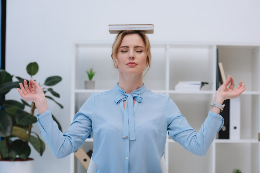 Business woman meditating with a book on her head