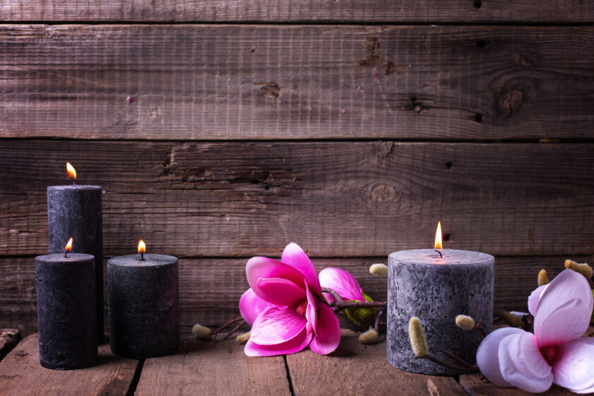 Still life wellness layout. Black burning candles and pink magnolia flowers on wooden rustic background. Selective focus. Place for text.