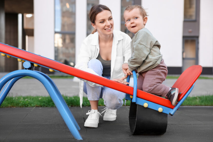 Happy nanny and cute little boy on seesaw outdoors