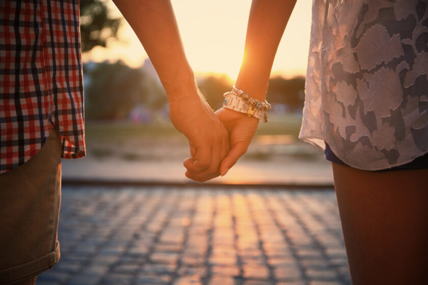 Closeup of loving couple holding hands while walking at sunset