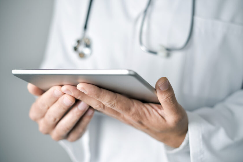 closeup of a young caucasian doctor man wearing a white coat using a tablet computer