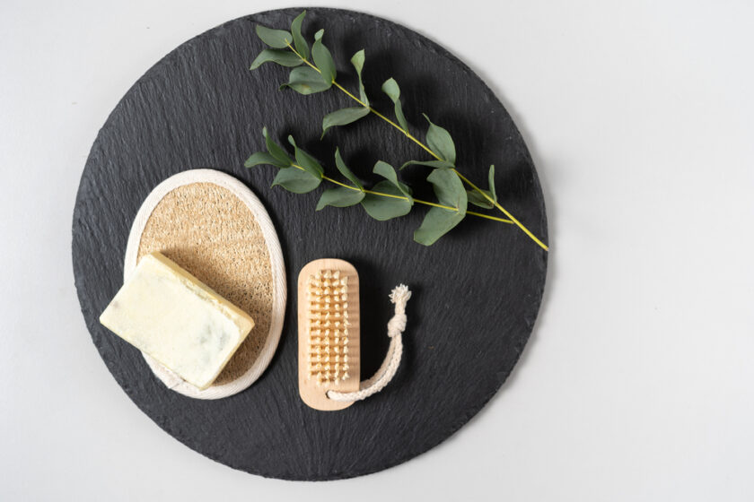 Concept of plastic free and bio decomposable objects. Flat lay, top view of natural bathroom supplies, nail brush, luffa sponge, solid soap, eucalyptus plant on plate against copy space background
