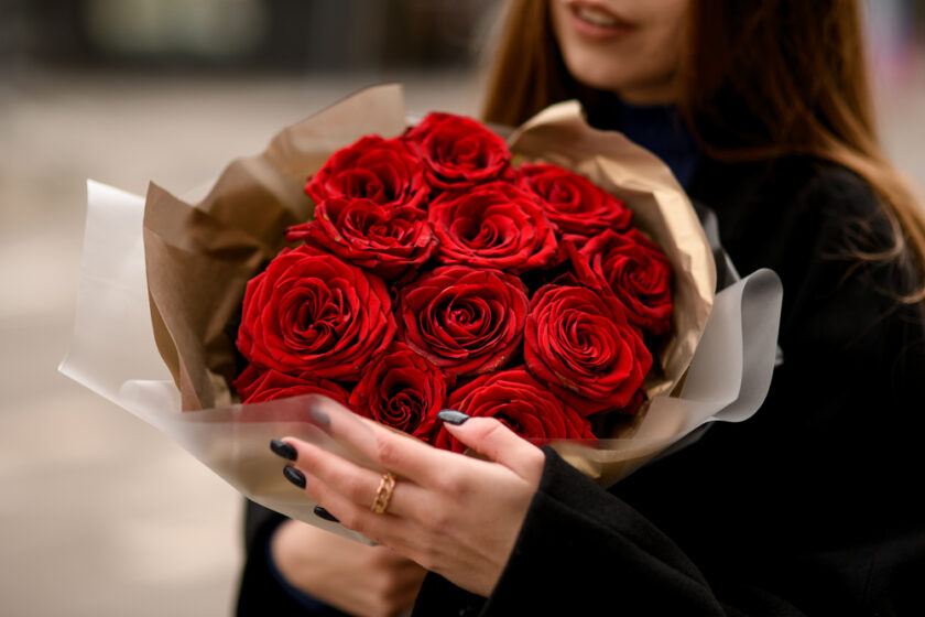Selective focus of beautiful bouquet with red roses for Valentine's Day wrapped in brown paper in woman's hands. Female with red flowers bouquet. Cropped shot