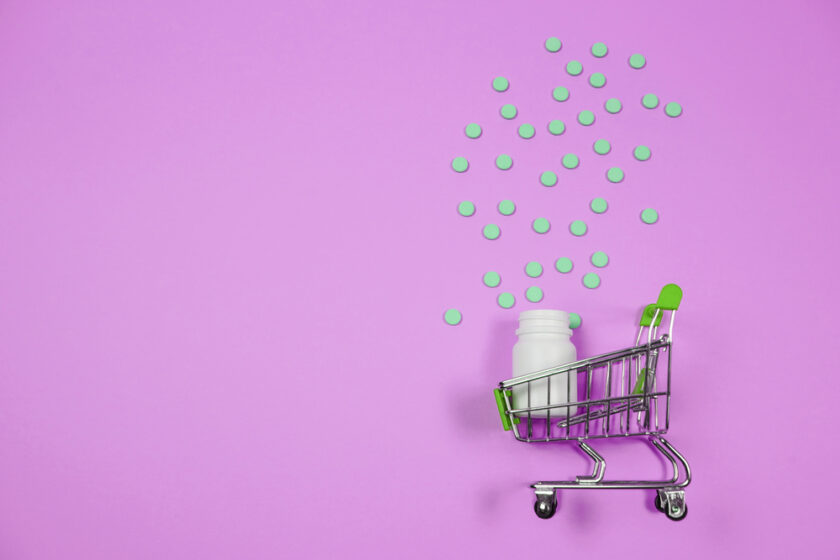 Pills in shopping cart on pink background. 