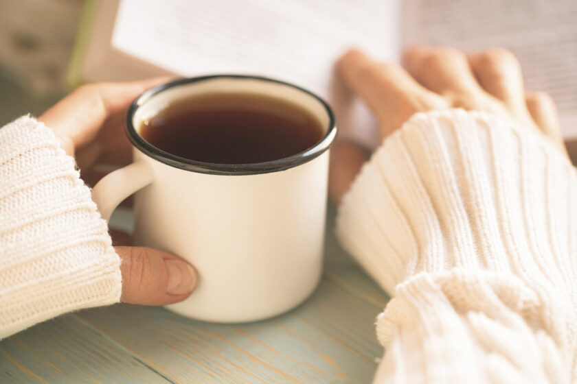 Girl reads book and drinks tea on window sill during winter holidays. Cosy home atmosphere.